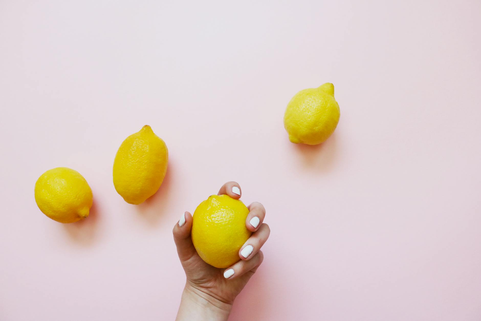 A hand holding a fresh lemon against a soft pink background, symbolizing sensuality and new beginnings