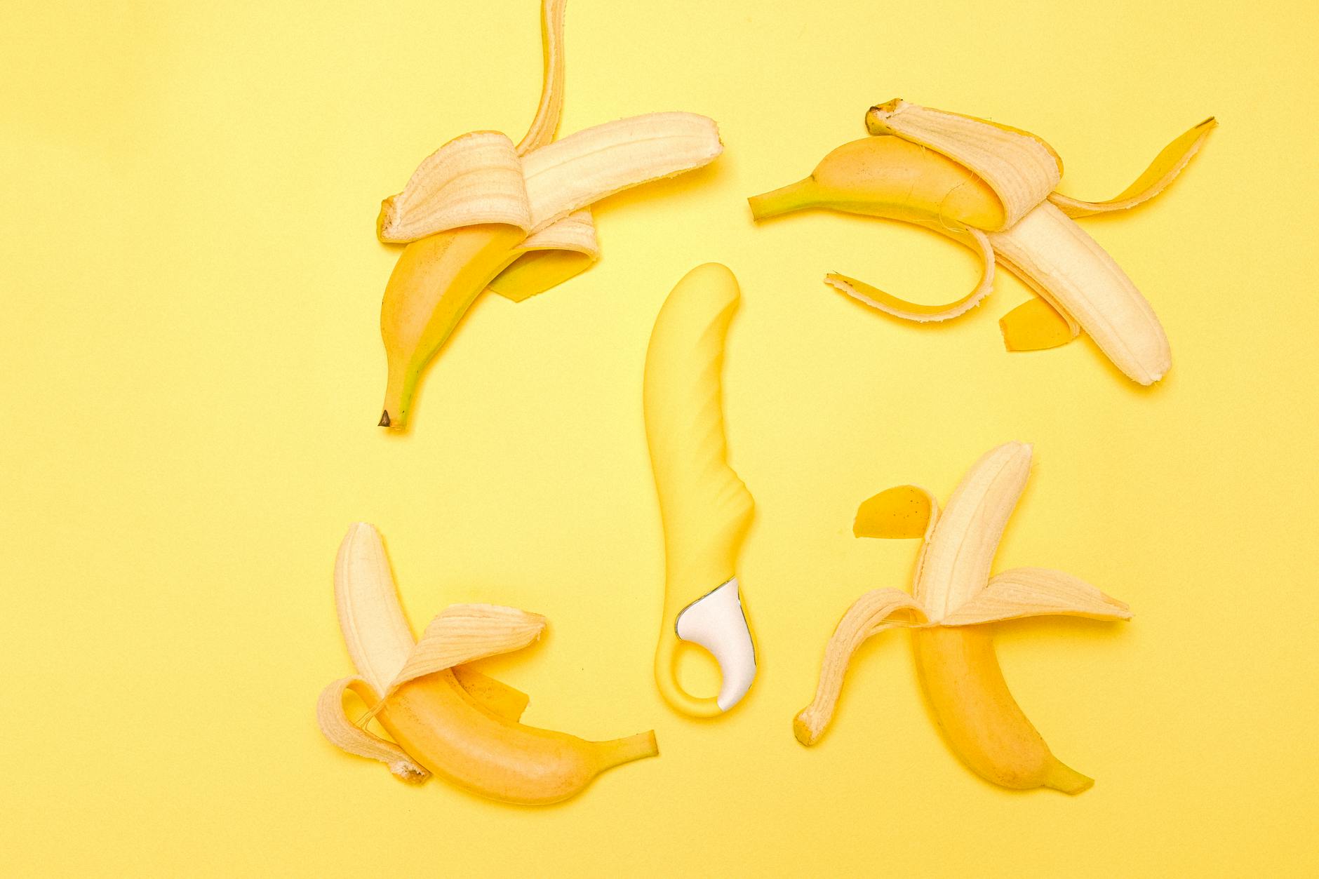 Yellow lemon vibrator surrounded by peeled bananas on a bright yellow background