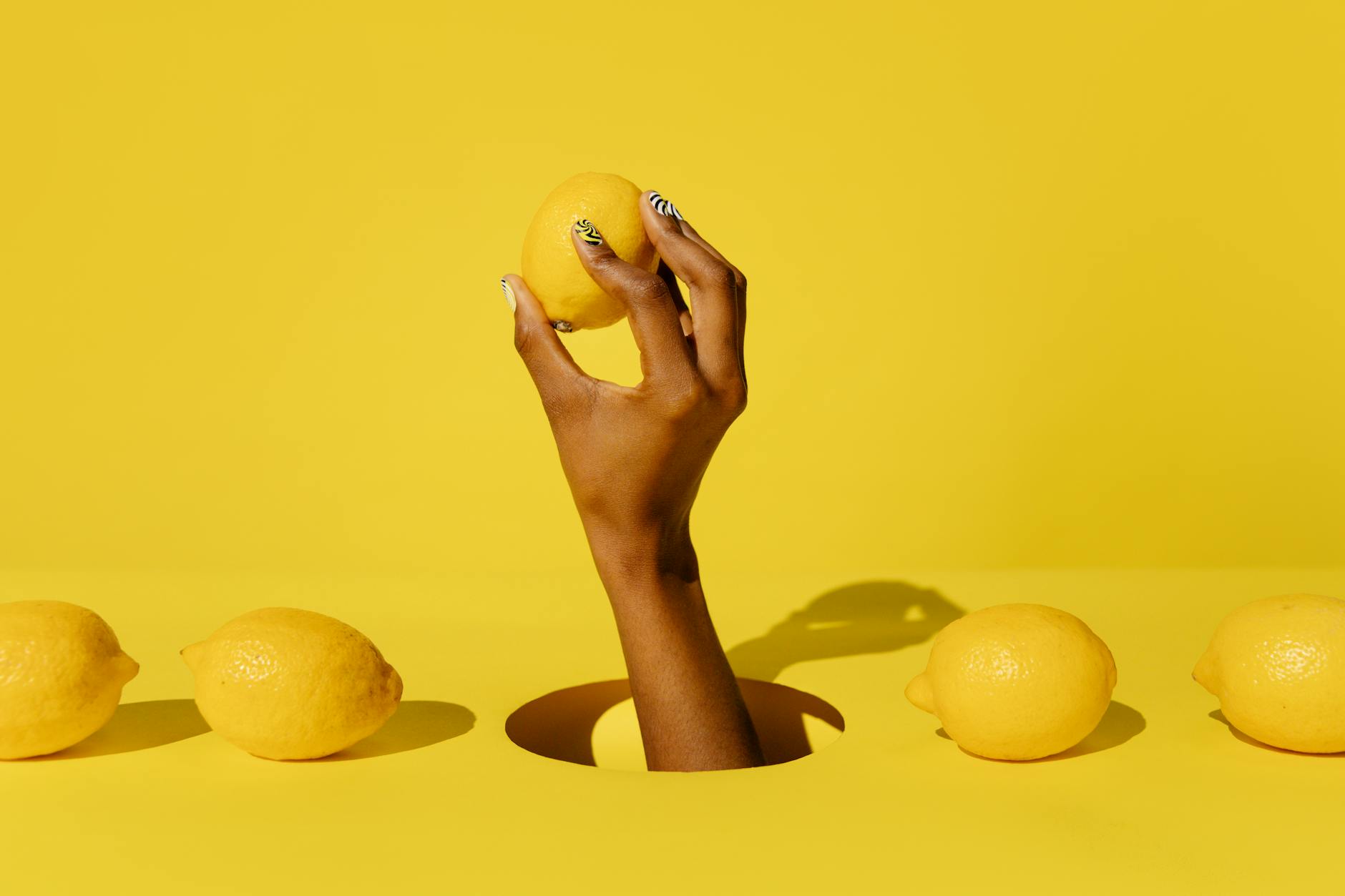 A hand holding a fresh lemon against a bright yellow background, symbolizing sensitivity and renewal