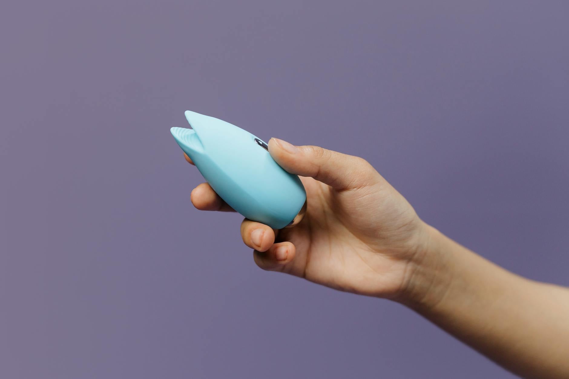 A lemon clitoral vibrator held in hand against a solid purple background, promoting self-love and travel-friendly pleasure.