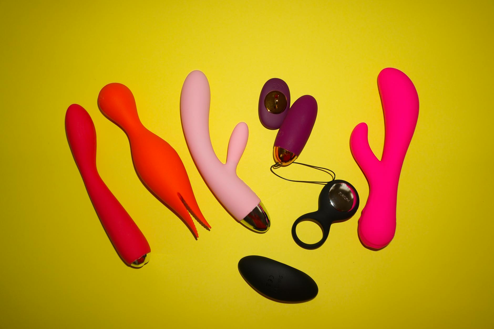 Colorful sex toys arranged on a bright yellow surface, showcasing various pleasure device options